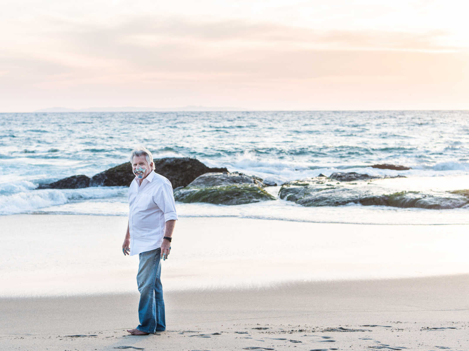 man walking along the shore with birthday cake all over his face