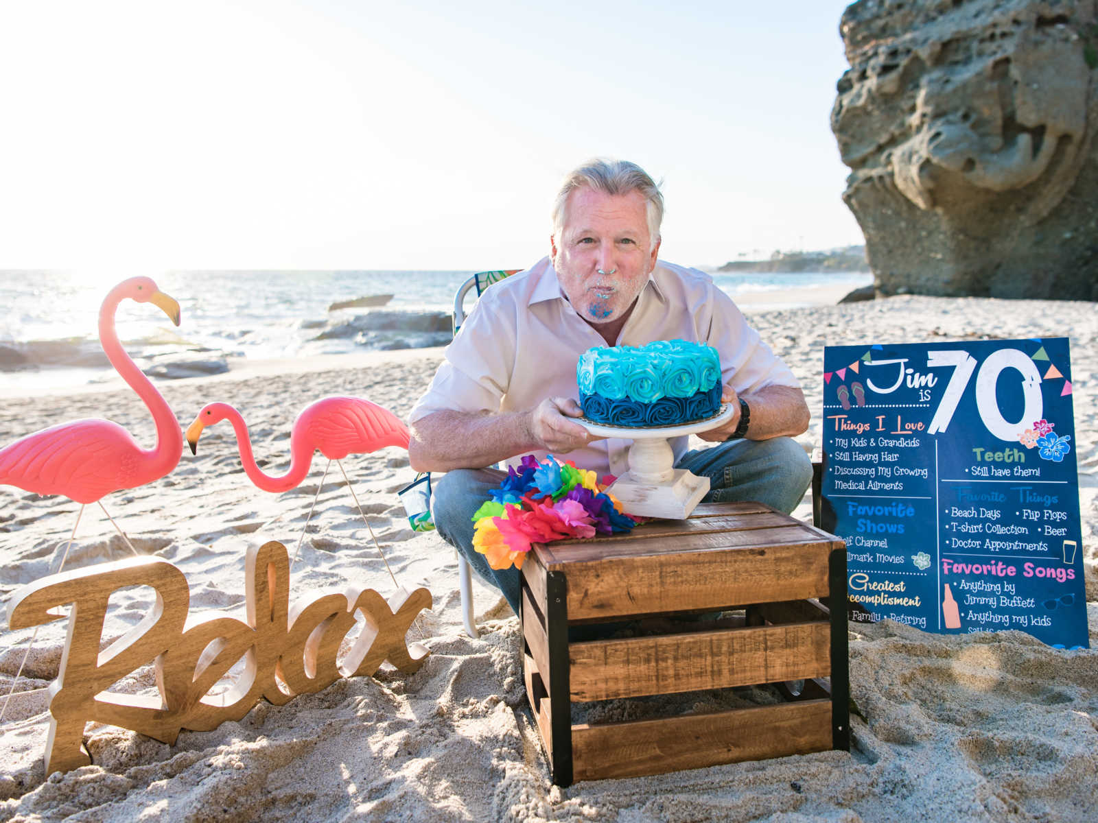 man with a mouthful of birthday cake and blue frosting all over his face on the beach