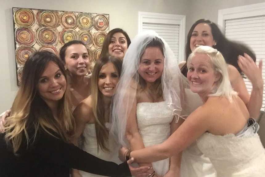 seven woman gathered closely in wedding gowns in a home