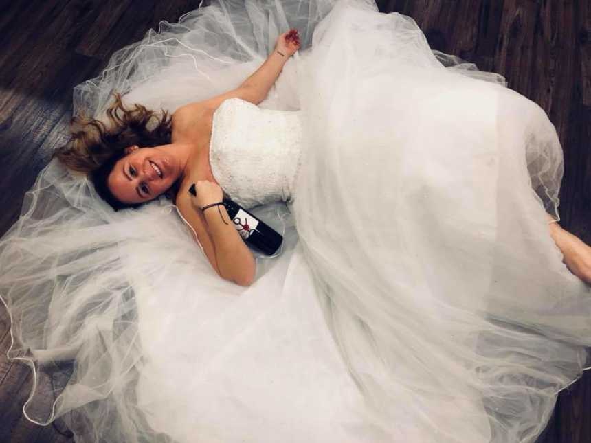 woman lying on the ground in a wedding dress with a bottle of wine held tightly to her chest