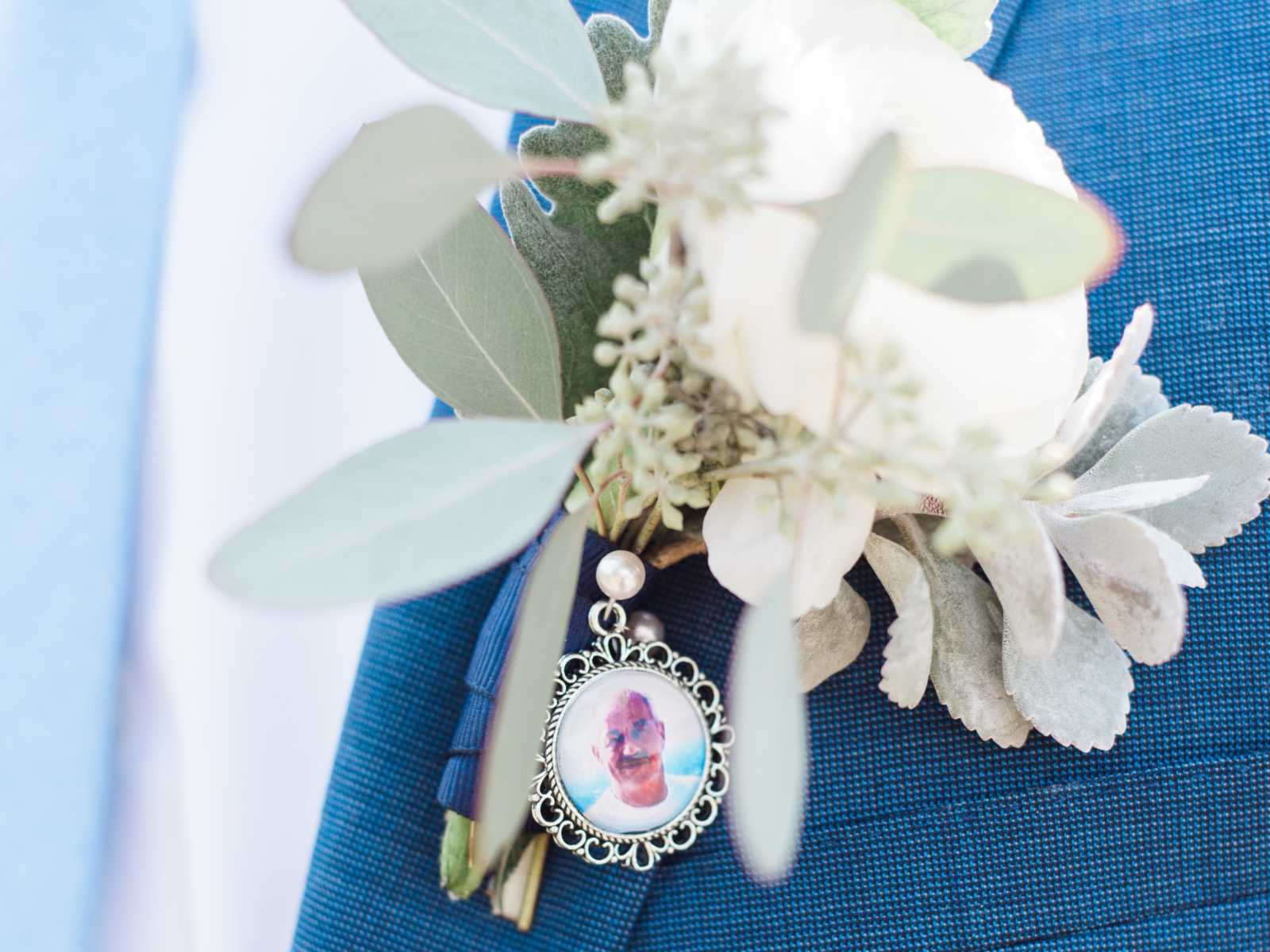 grooms white boutonniere with a charm of brides late father dangling off of it 