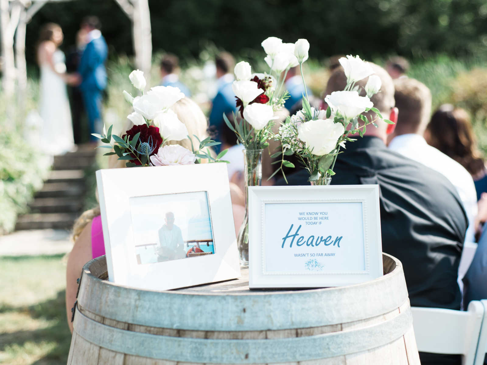 wooden barrel with flowers and picture frame of deceased father with wedding ceremony in the background