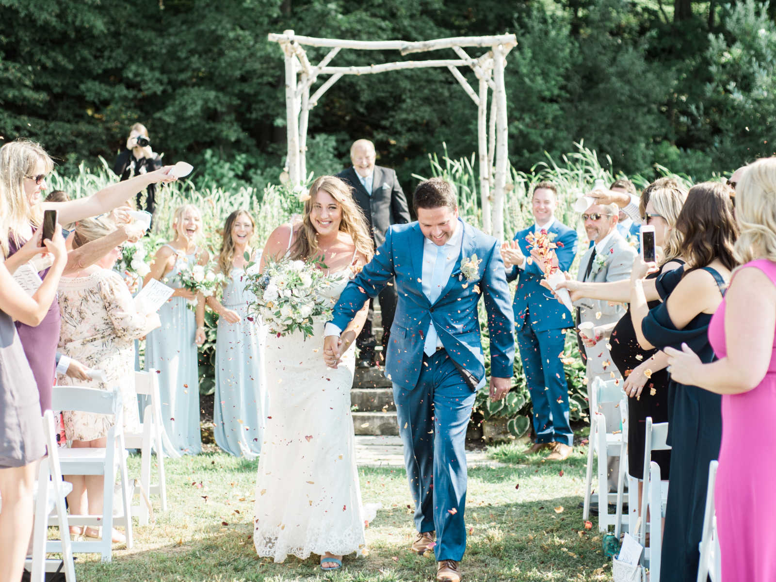 bride and groom hand in hand walking down the aisle showered in flowers by smiling guests