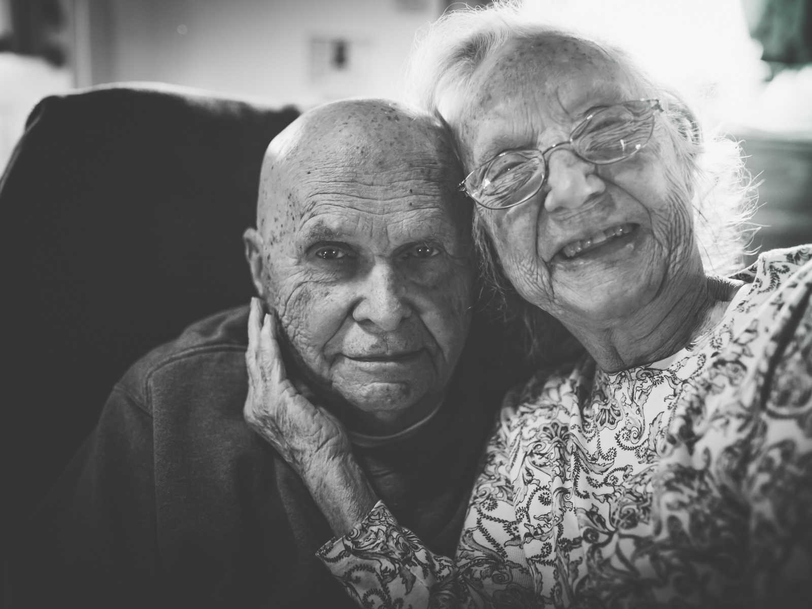 elderly couple smiling as wife sits on husbands lap