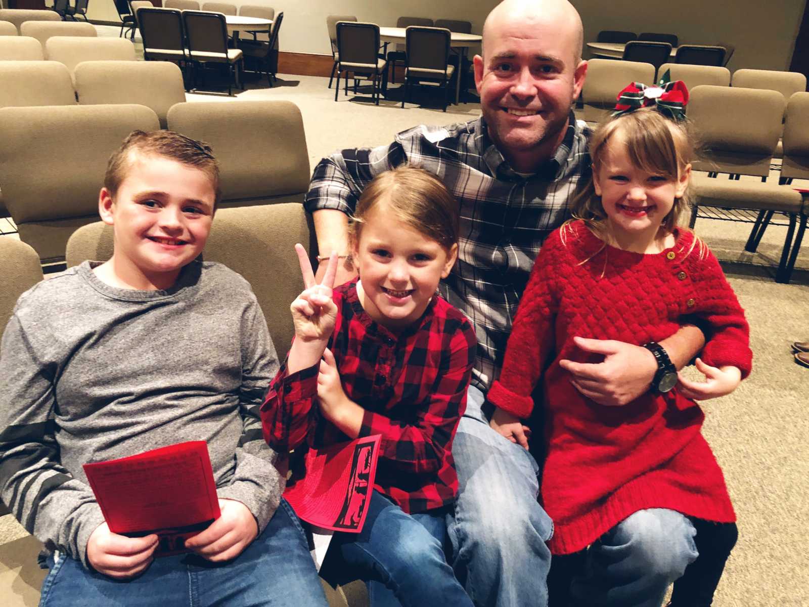 Widowed man smiles while kneeling with stepdaughter on knee next to other stepdaughter and actual son sitting to the left