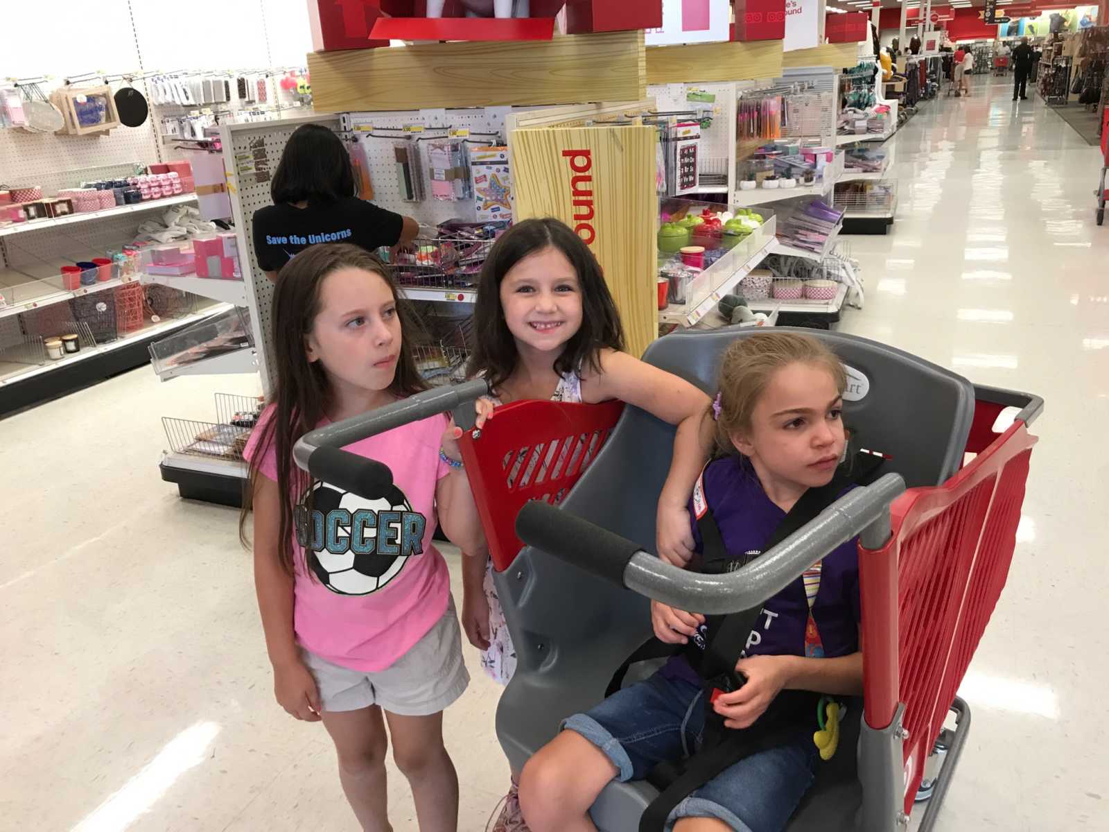 young girl with terminal illness sits in target shopping cart with young girls standing next to her in target aisle