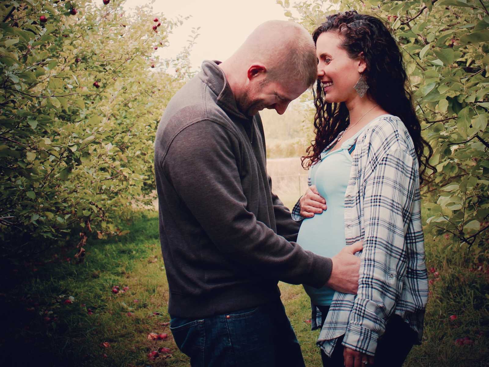 pregnant woman smiles and holds belly as man holds her waist and smiles at her stomach