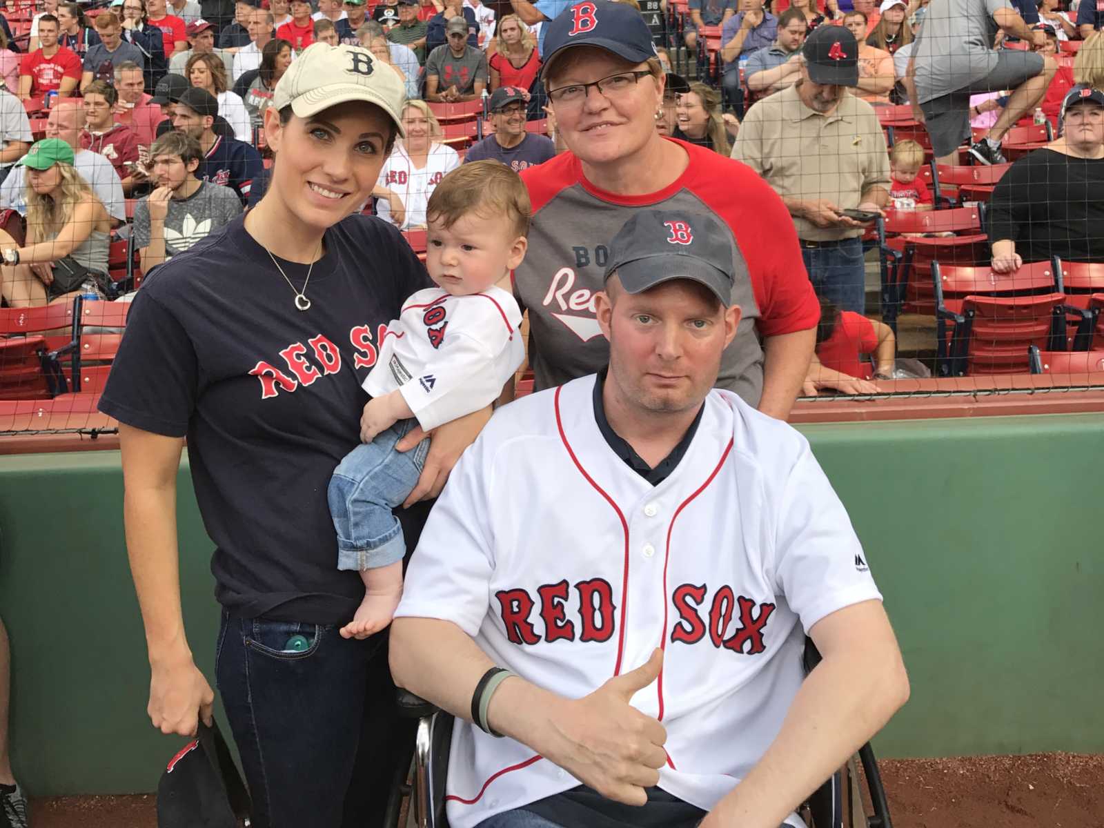 brain cancer patient gives thumbs up on red sox field with wife, son, and mother behind him