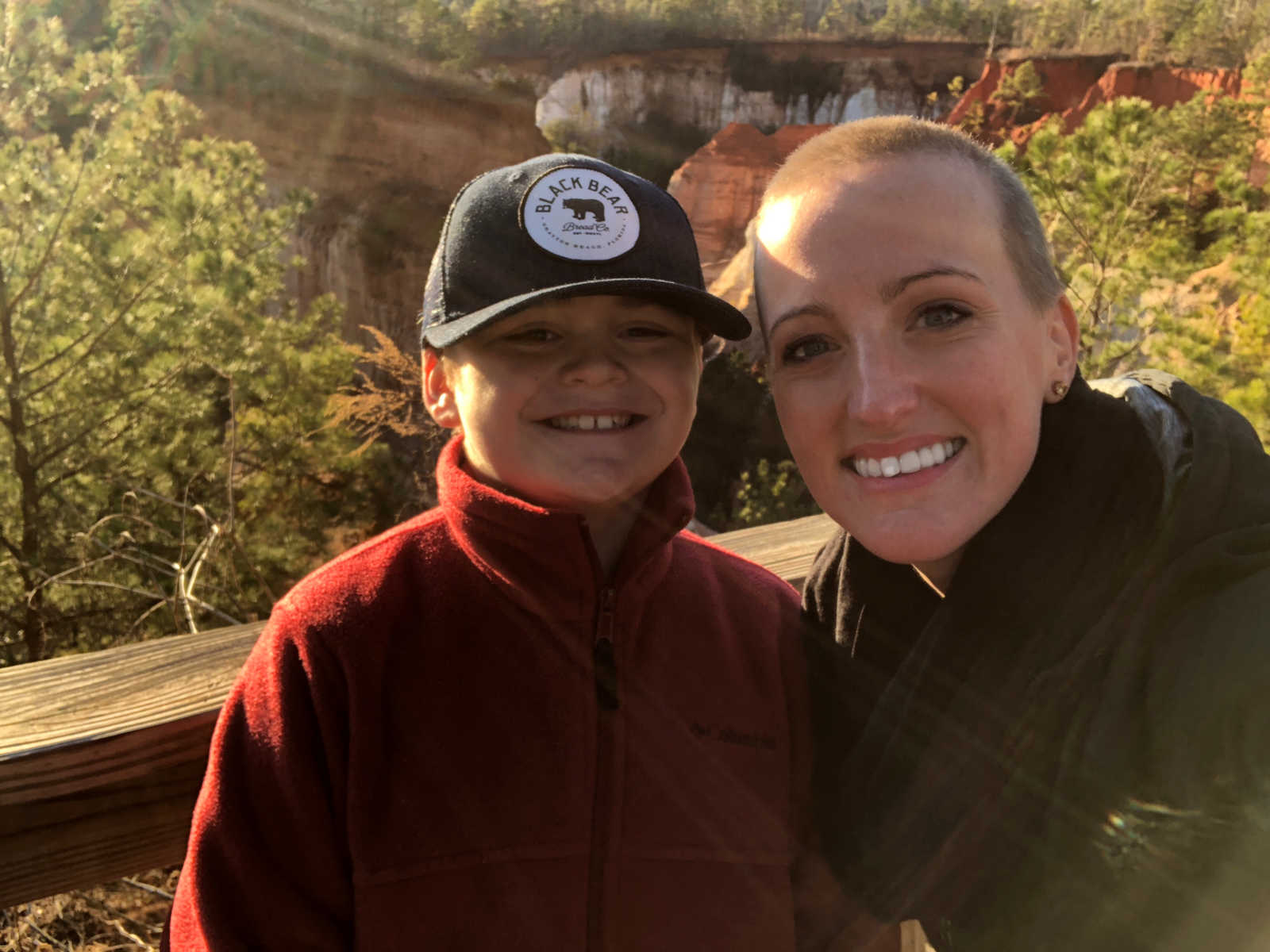woman smiles in selfie with young stepson with cliffs and trees in background