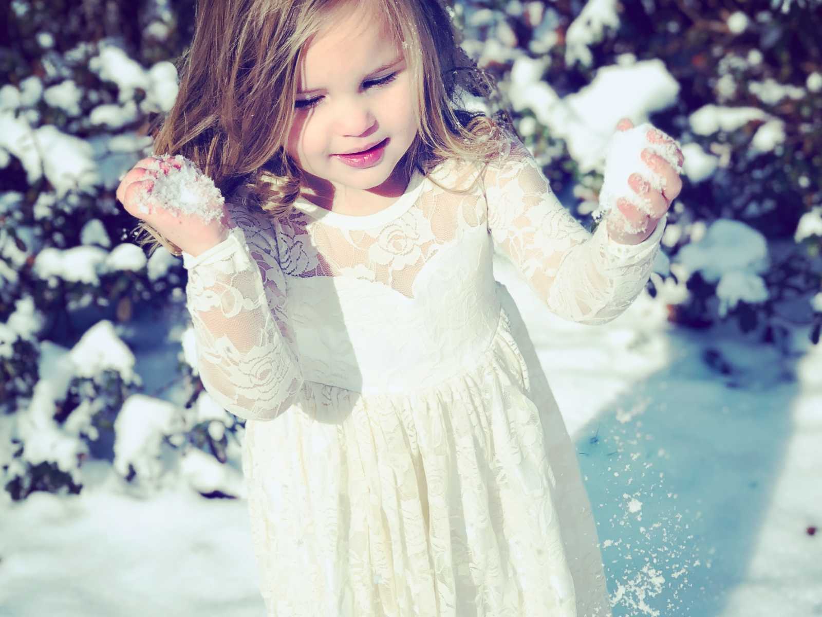 young girl in white floral lace dress with fists full of snow