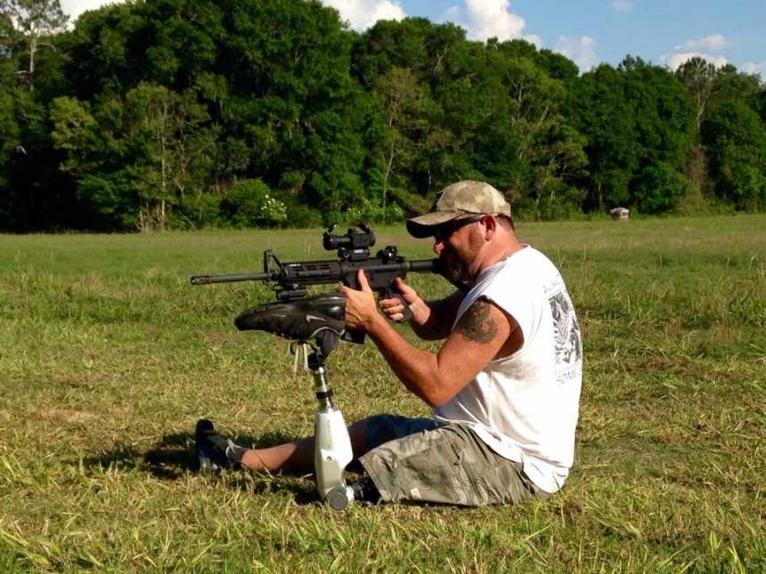 army vet sitting in field shooting gun and propping it up with prosthetic leg