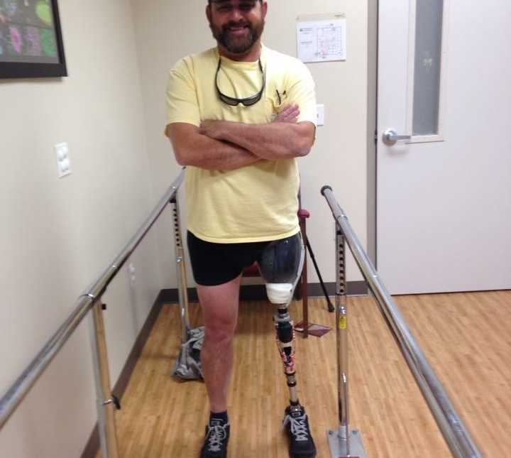 veteran wearing yellow t-shirt at physical therapy with a prosthetic leg standing with arms crossed smiling