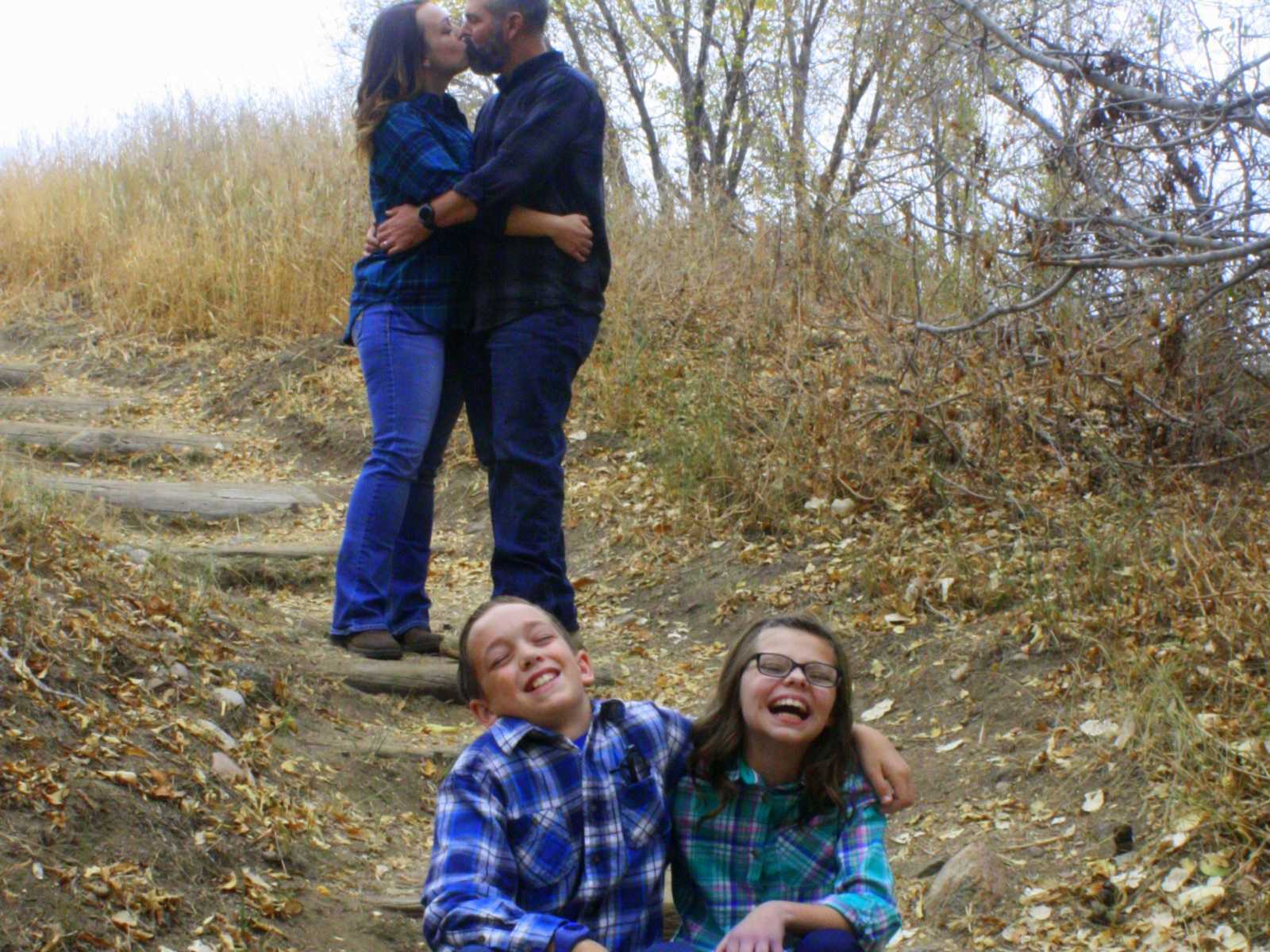 man and woman kiss on stone steps while son and daughter sit on steps below with arms around each other smiling
