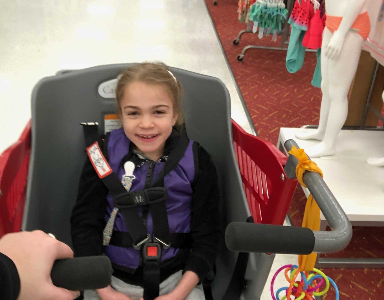 young girl with terminal illness looks up smiling while she is being pushed in target shopping cart