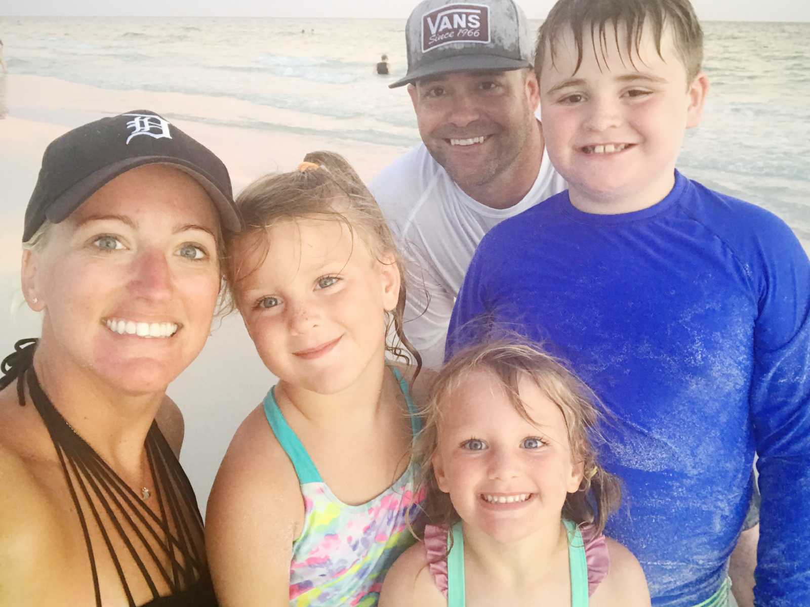 widowed mother smiles in selfie on beach in bathing suits next to two daughters and widowed boyfriend and his son