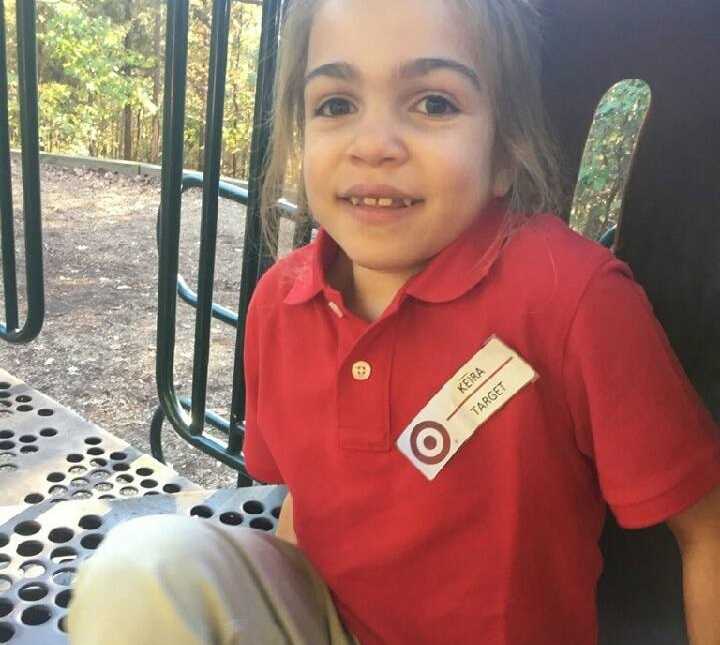 young girl with terminal illness sitting on playground structure in red shirt and khakis with target name tag on