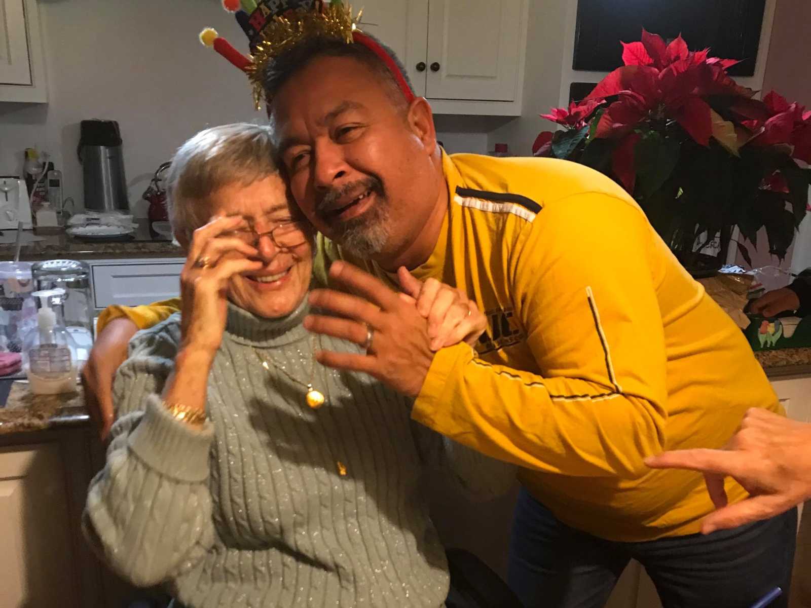 Man with birthday headband on leans over to give woman with dementia a hug