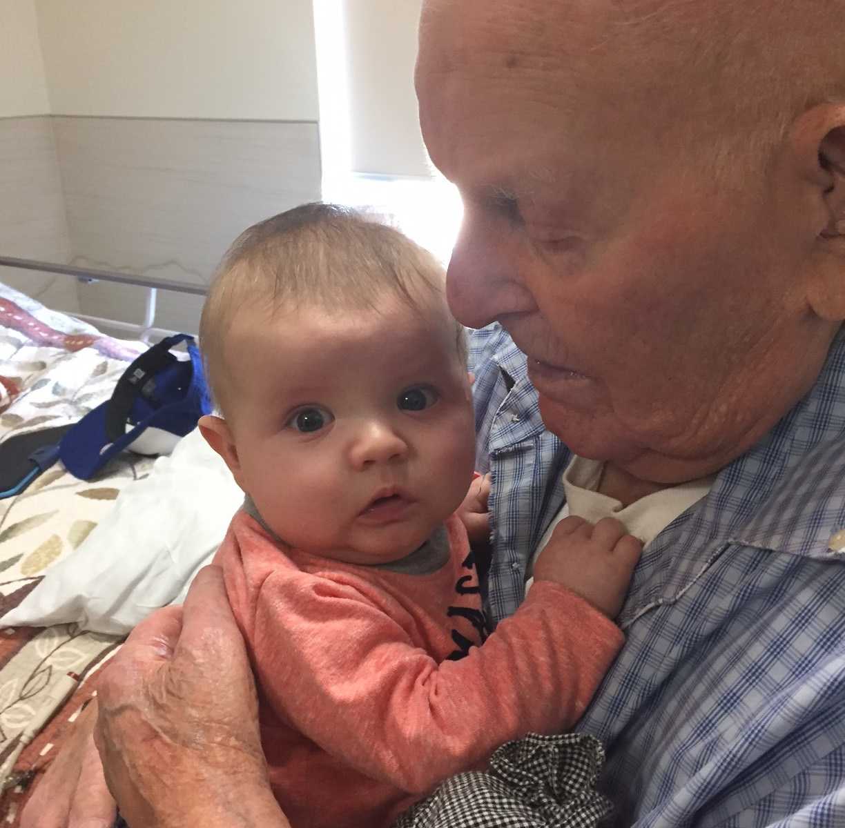 close up of oldest man in Canada looks down while holding great-great-grandson to chest and baby looks to side