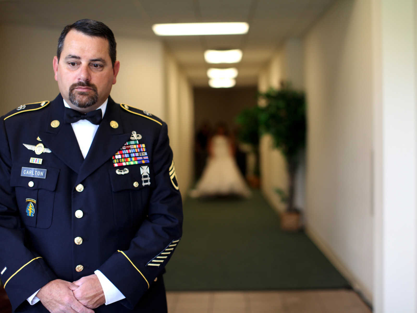 army vet in uniform standing in hallway with back turned and daughter walking towards in wedding gown