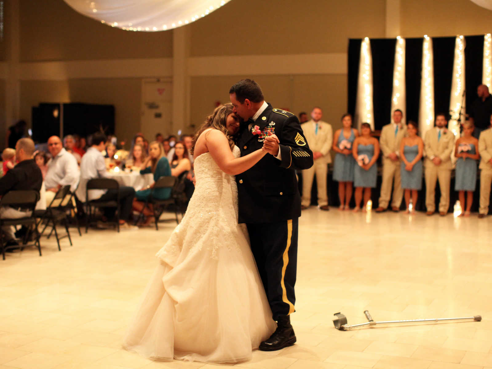 recovered soldier dances with daughter at wedding with his crutch on the ground and wedding guests watching