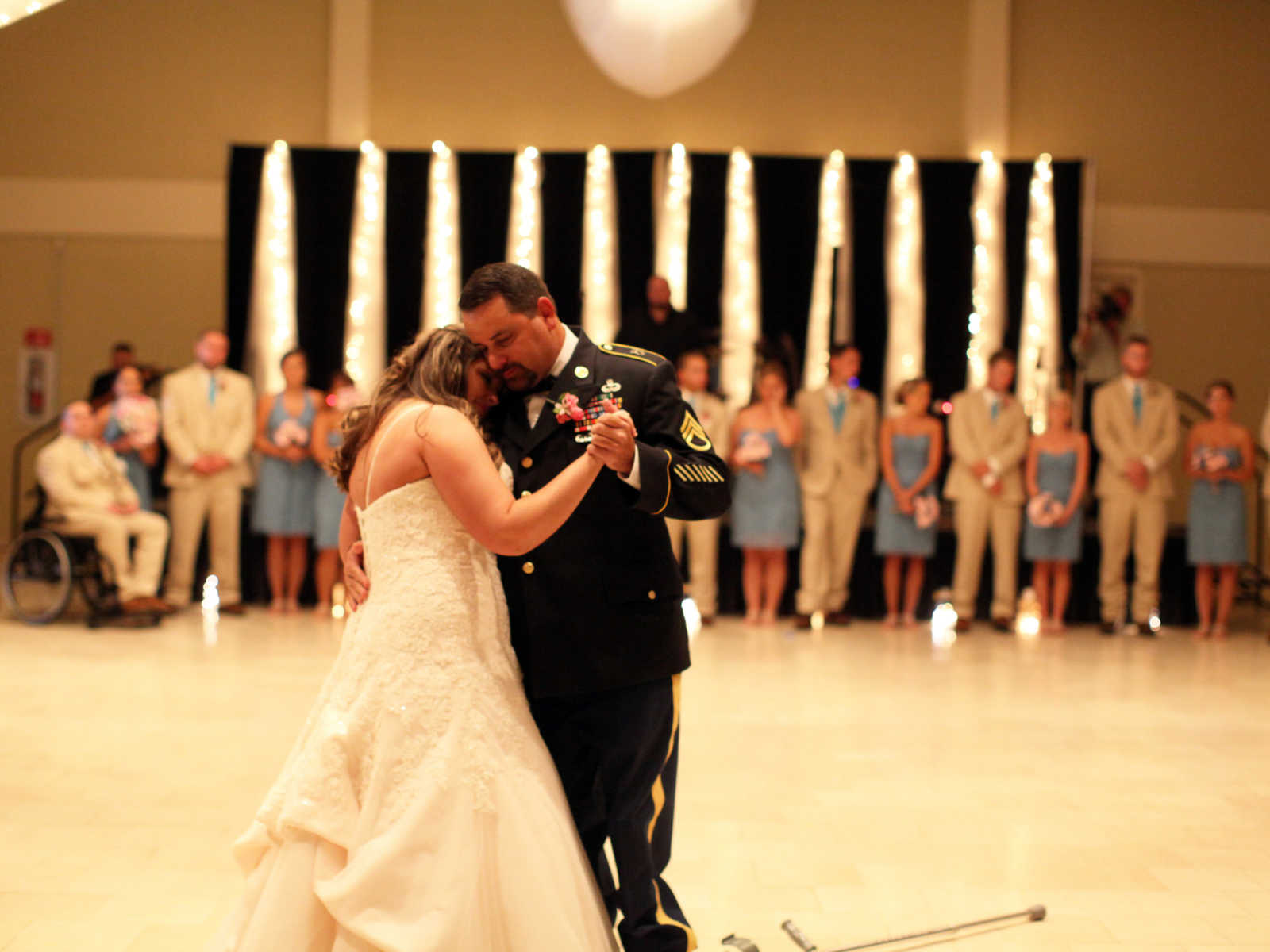 bride has head on fathers shoulder as they dance at wedding with wedding party watching in background