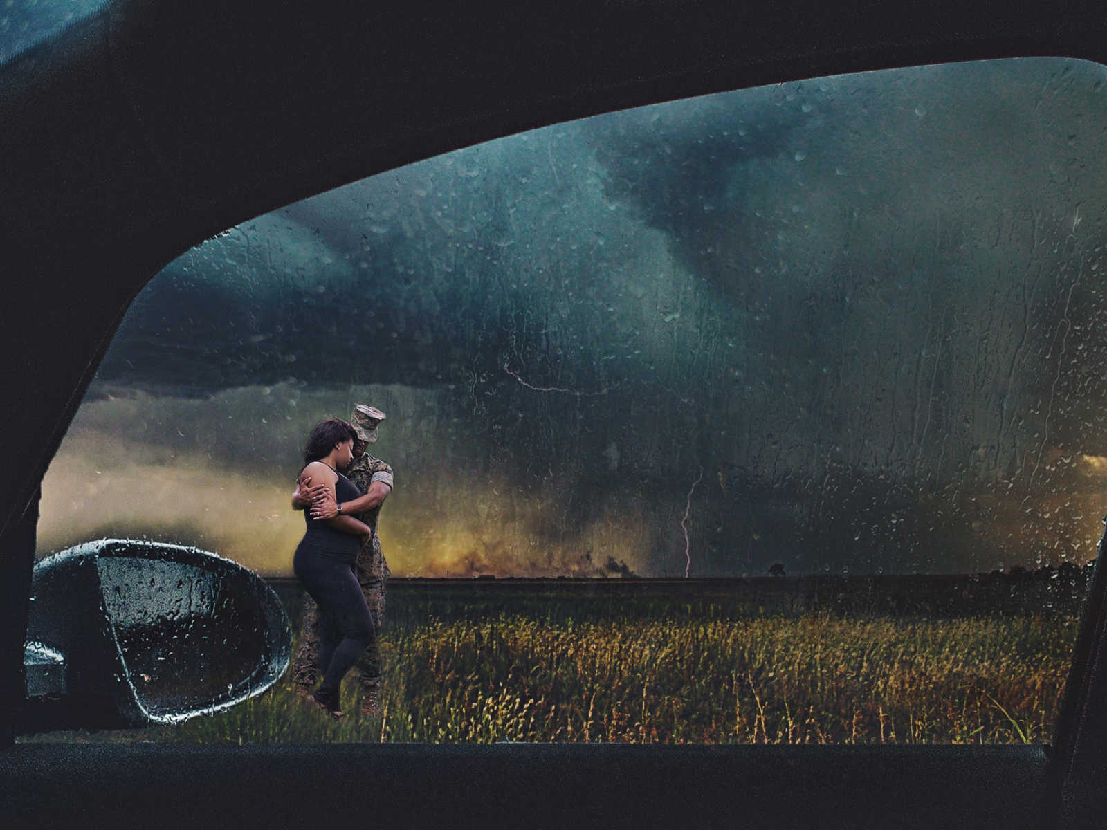 through a car window marine husband is holding wife in a field during a thunder storm