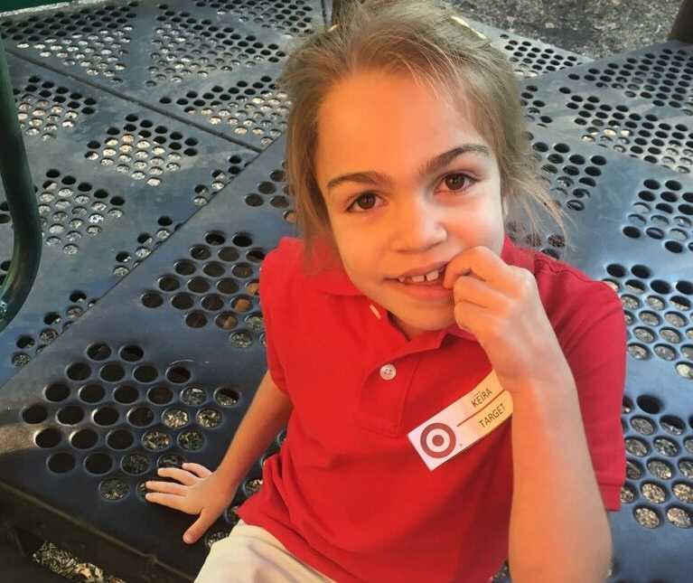 young girl with terminal illness touches her mouth while sitting on steps of play structure