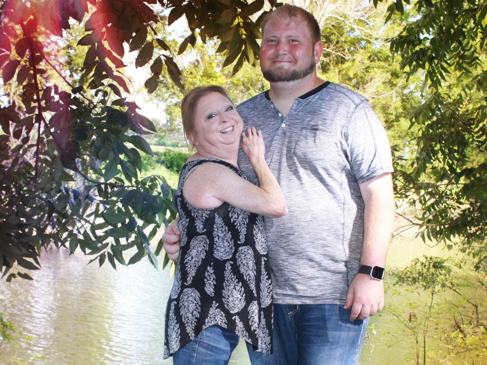 disabled couple smiling with arms wrapped around each other in front of body of water