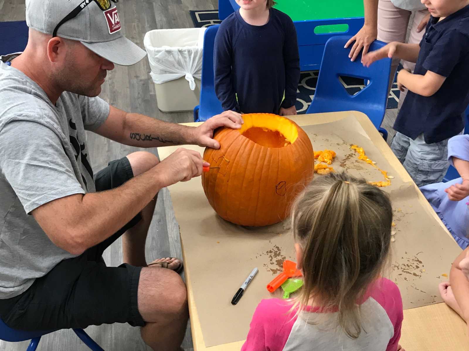 widowed man sitting at table with little kids surrounding while he carves a pumpkin