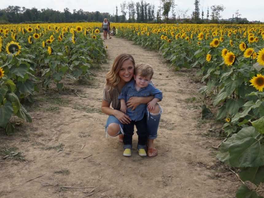 Mother crouches down to hold toddler who cries in stores in sunflower field