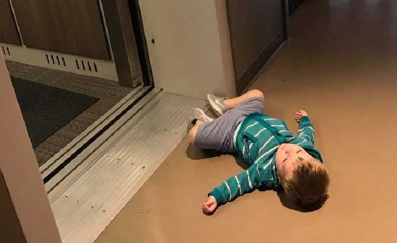Toddler lays on floor next to open elevator