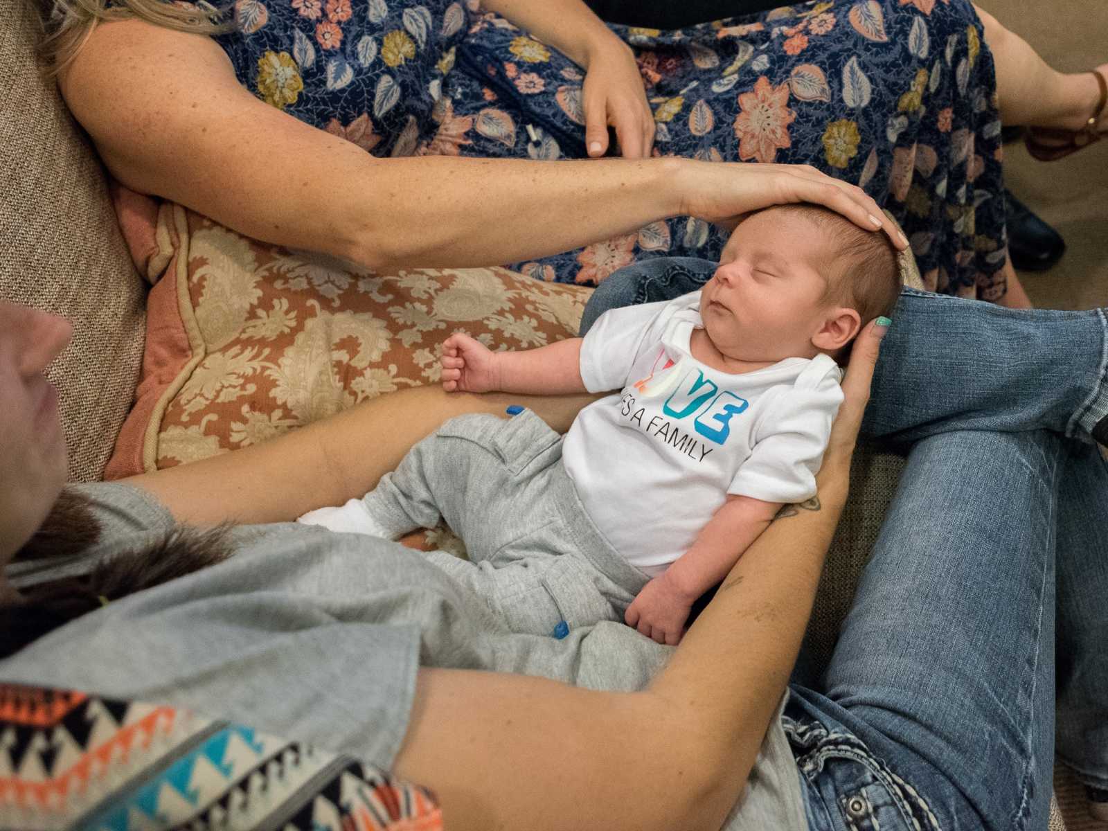 aerial view of birth mother holding son in her lap while adoptive mother has hand on sons head