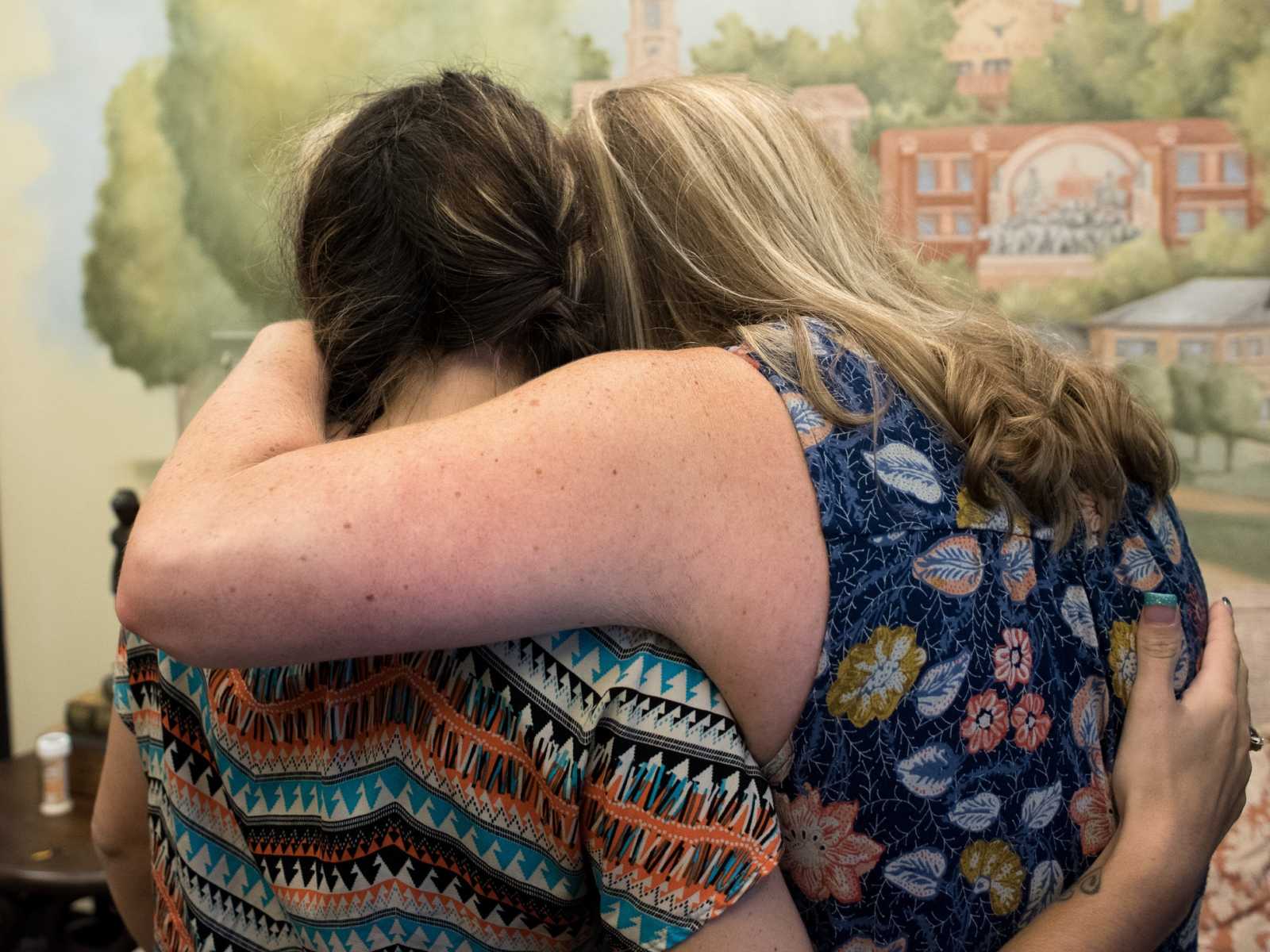 view from the back of birth mother and adoptive mother with arms wrapped around each other 