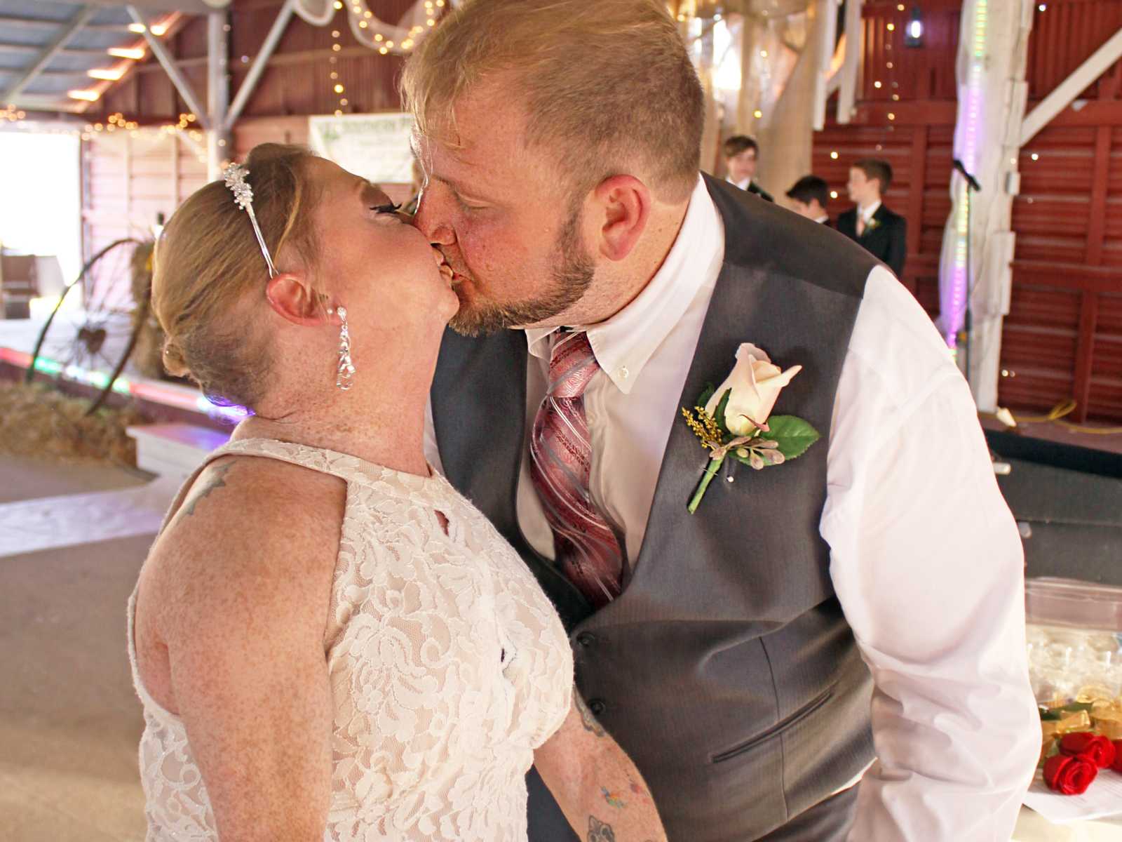 disabled couple share a kiss at barn wedding with young boys in suits in background