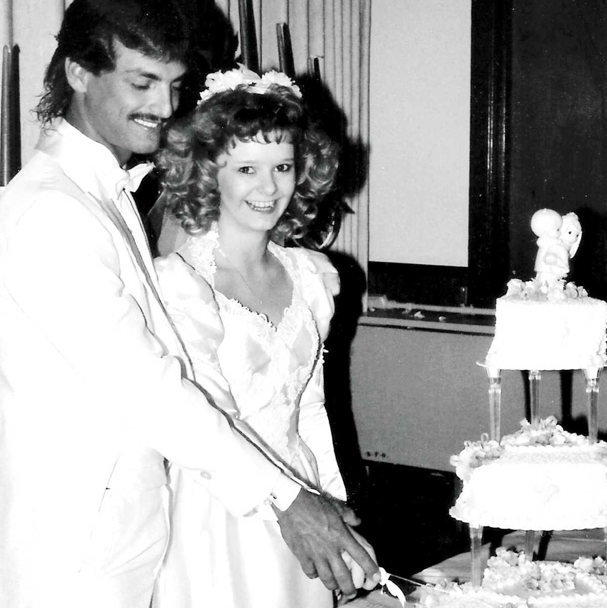 bride and groom hand in hand cutting their wedding cake in black and white