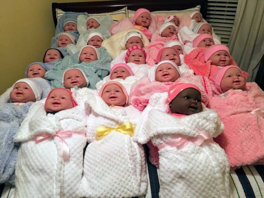 rows of baby dolls of different skin colors swaddles in blue, white, and pink blankets with bow tied around them