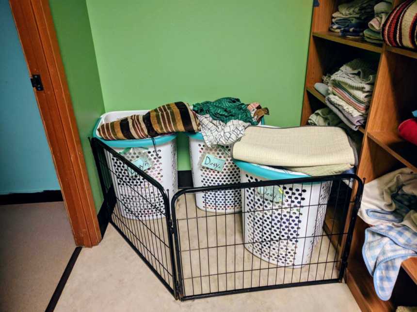 laundry baskets loaded to the tip corralled in by dog fence with shelves of blankets to the right