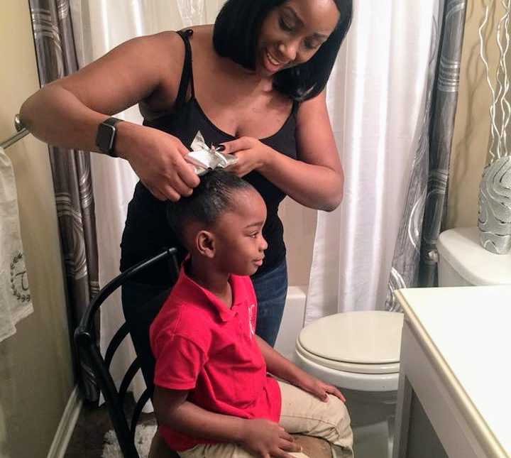 daughter sits on stool in bathroom while mother puts white bow in her hair