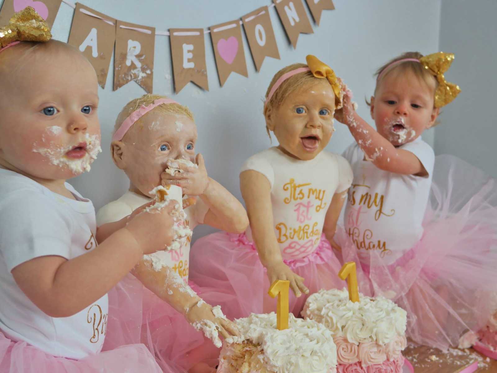 two cakes that resemble real babies sit in between two infants in gold bow and pink tutu with cake on their face
