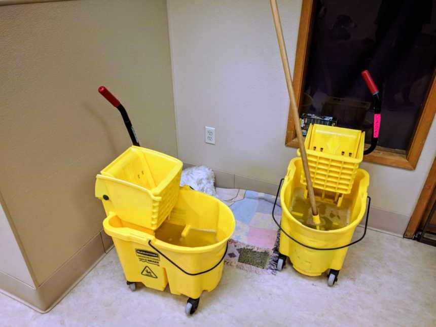 two yellow roller buckets with a mop in one in a hallway