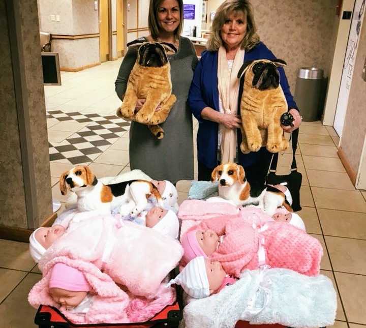 two women in hallway holding large stuffed pugs with two carts of baby dolls and stuffed beagles in front of them