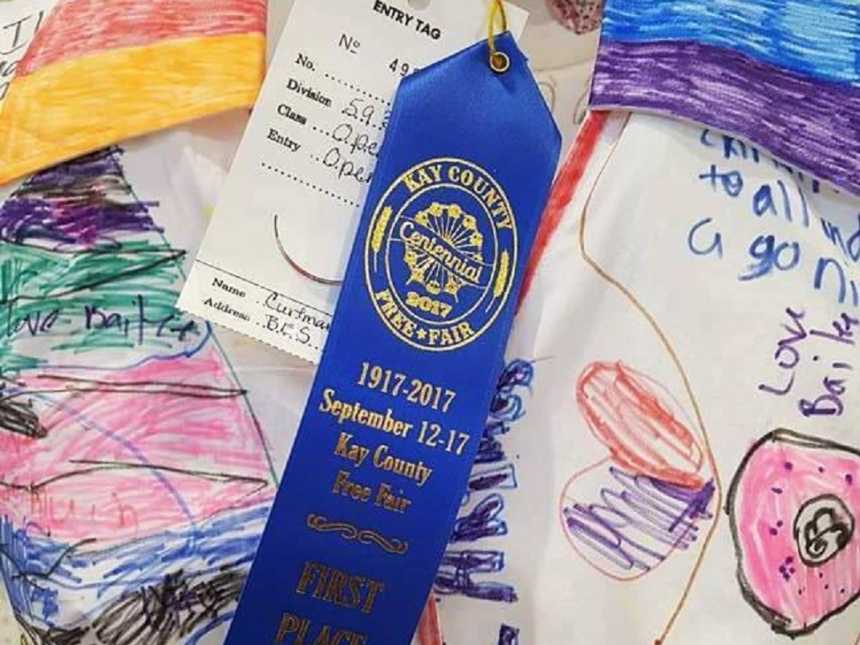 close up of first place blue ribbon on teachers white dress covered in students drawings