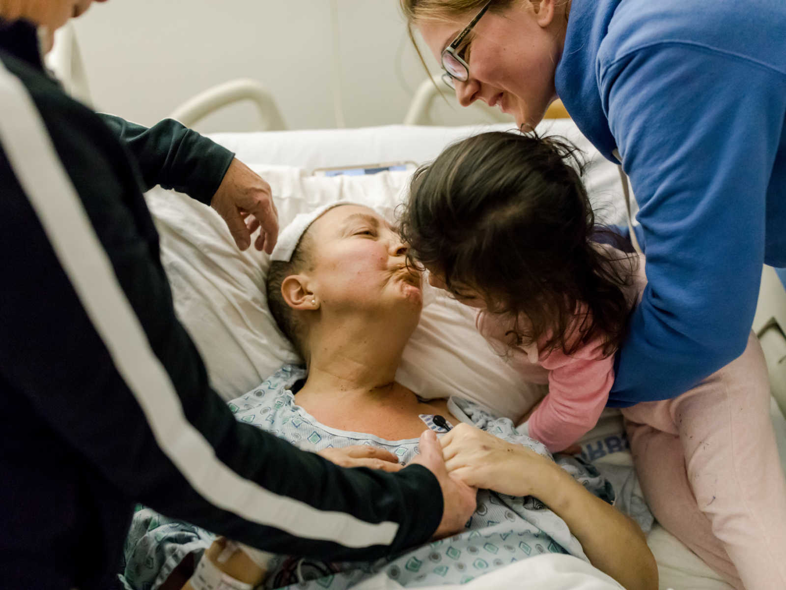 Woman with non-hodgkin's lymphoma gives toddler a kiss who is being help by woman's sister