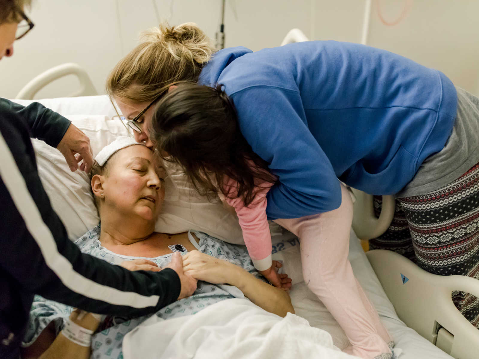 Non-hodgkin's lymphoma patient receives kiss on forehead from sister who is holding toddler and mother watches