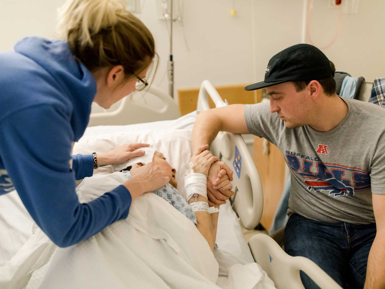 Non-hodgkin's lymphoma patient lies in hospital bed holding brothers hand while sister holds on to her