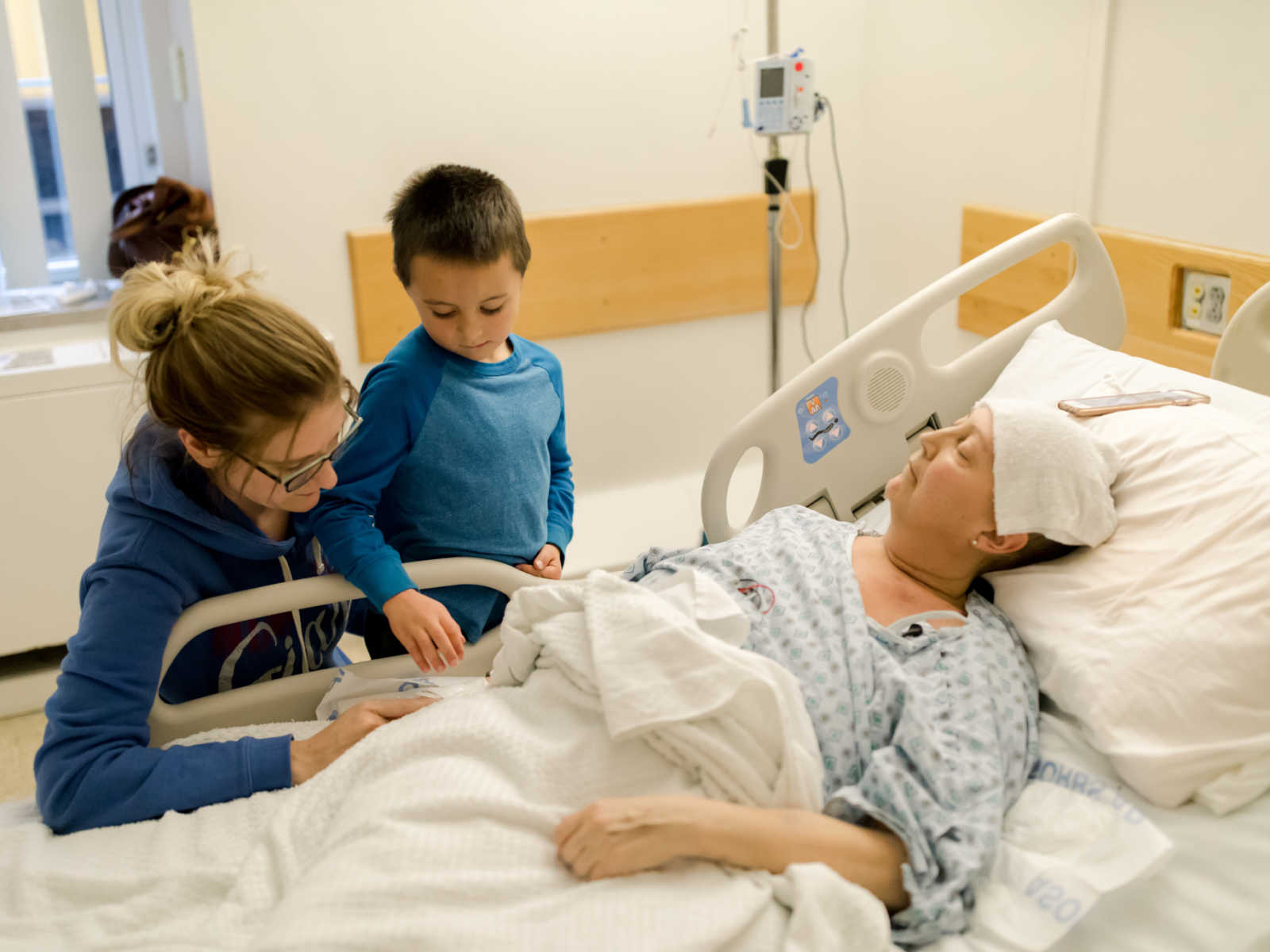 Non-hodgkin's lymphoma patient lies in hospital bed while sister and little boy watch over her