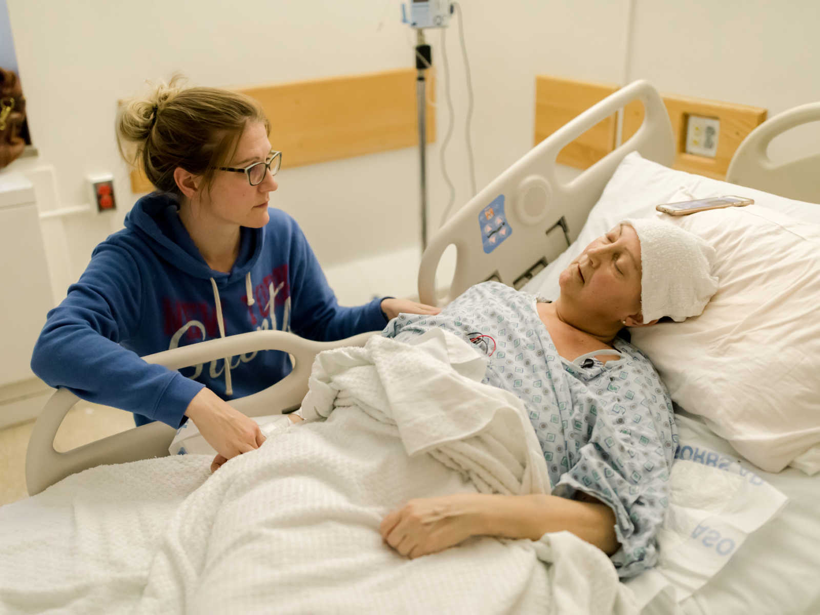 Woman sitting next hospital bed where her sister who suffers from non-hodgkin's lymphoma is sleeping