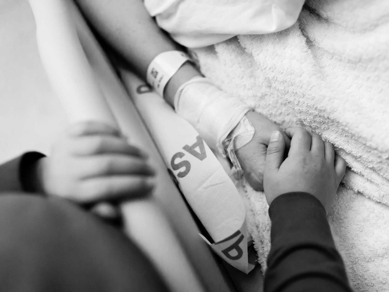 Close up of non-hodgkin's lymphoma patient holding the hand of another in hospital bed