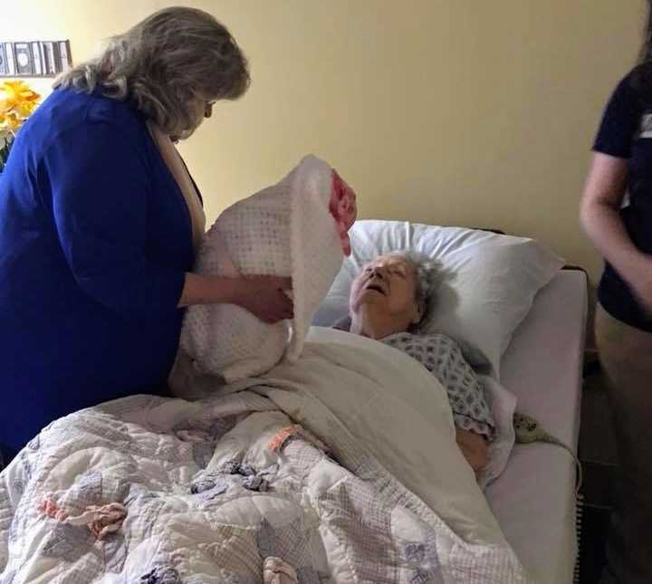 alzheimer patient lying in bed looks up seeing a woman holding a swaddled baby doll over her