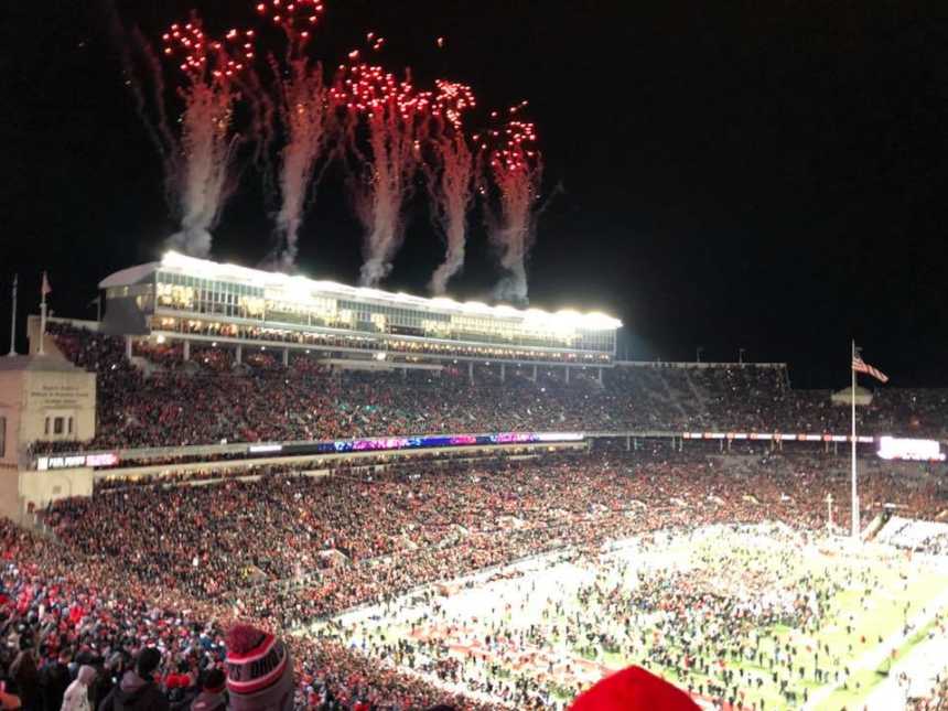 packed football stadium shooting off fire works and people rushing the field